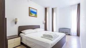 Une chambre d’hôtel avec un lit, une table de chevet, une lampe, un tableau et une fenêtre avec des rideaux.