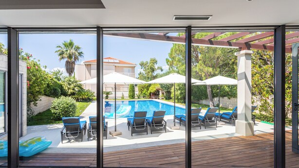 Un espace piscine extérieur moderne, doté de chaises longues et de parasols, entouré de verdure et offrant une vue dégagée sur un immeuble d’habitation en arrière-plan.