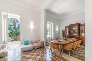 Un vaste espace de vie comprenant un canapé, une table à manger et des chaises. Une grande fenêtre offre une belle vue sur les arbres et permet à la lumière naturelle d’entrer.