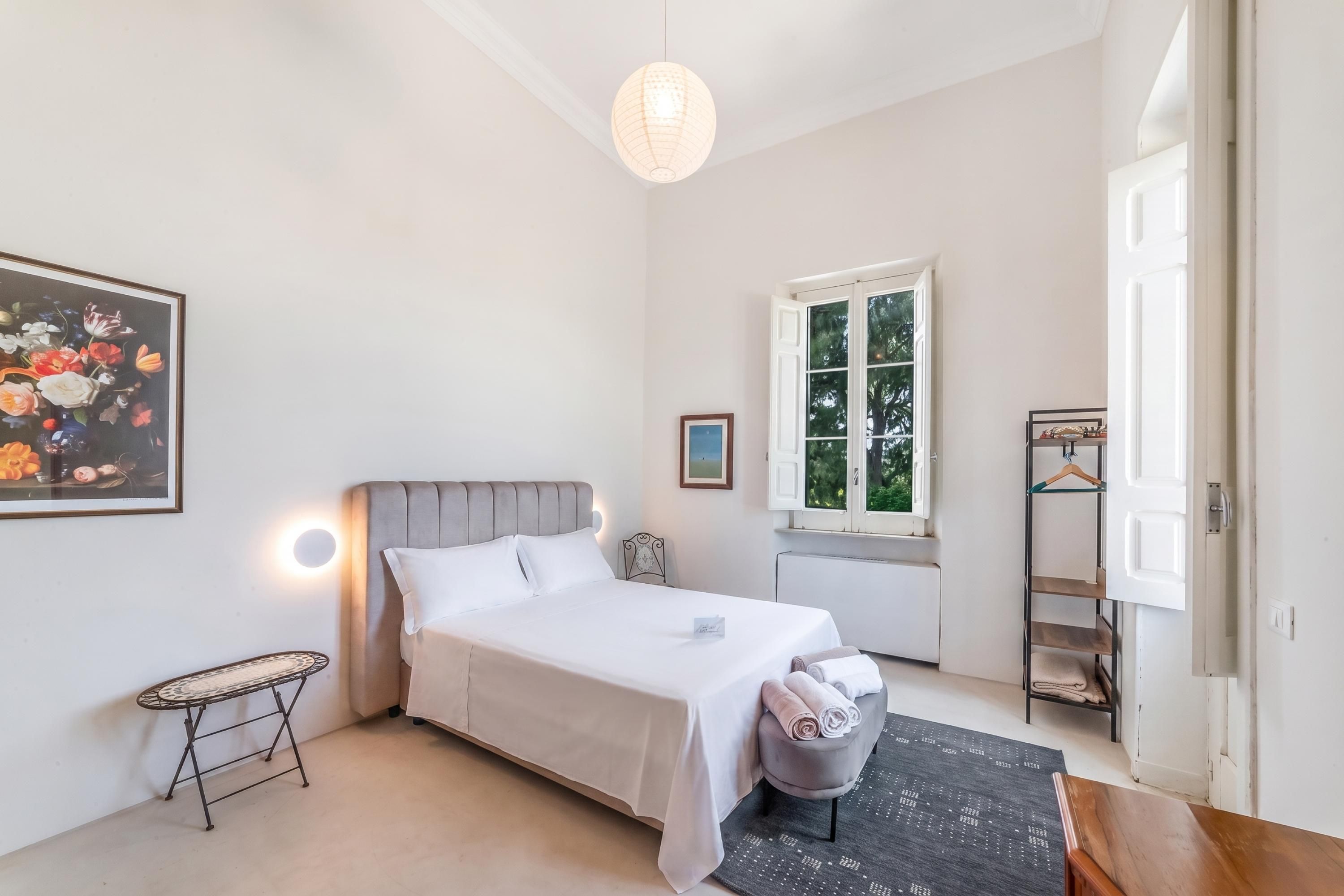 Una camera da letto con un letto, comodino, lampada e una finestra vista alberi.