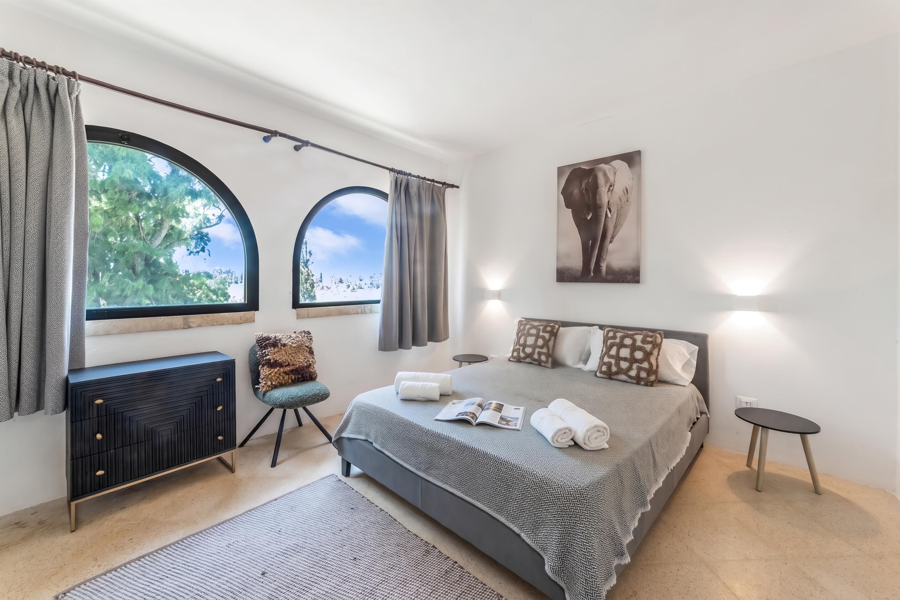 Une chambre moderne avec un grand lit, deux fenêtres, un radiateur, une petite table et un luminaire fixé au mur.