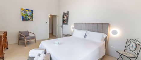 A hotel room with a large bed, a chair, a small table, and artwork on the walls.