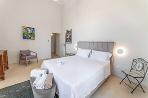 A hotel room with a large bed, a chair, a small table, and artwork on the walls. - Villa Vallone Luxury With Pool (Galatina)