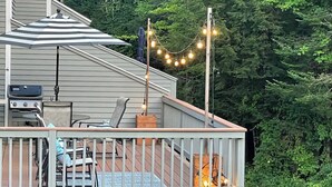 A covered outdoor deck with a grill, chairs, and string lights.