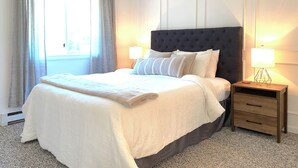 A neatly made bed with a dark headboard, two bedside tables with lamps, and a window with curtains.