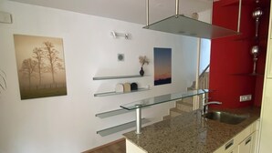 A modern kitchen with a granite countertop, stainless steel appliances, and a red accent wall. - Gemütliches Haus mit 2 Schlafzimmern im Zentrum von Kaprun mit Schönen Terrassen (Kaprun)