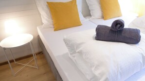 A neatly made bed with white and mustard yellow pillows, a grey towel, and a white bedside table. - Gemütliches Haus mit 2 Schlafzimmern im Zentrum von Kaprun mit Schönen Terrassen (Kaprun)