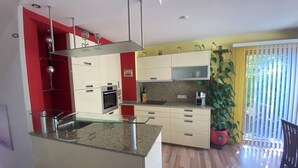 A modern kitchen with a central island, built-in oven, and a dining area with a large window. - Gemütliches Haus mit 2 Schlafzimmern im Zentrum von Kaprun mit Schönen Terrassen (Kaprun)