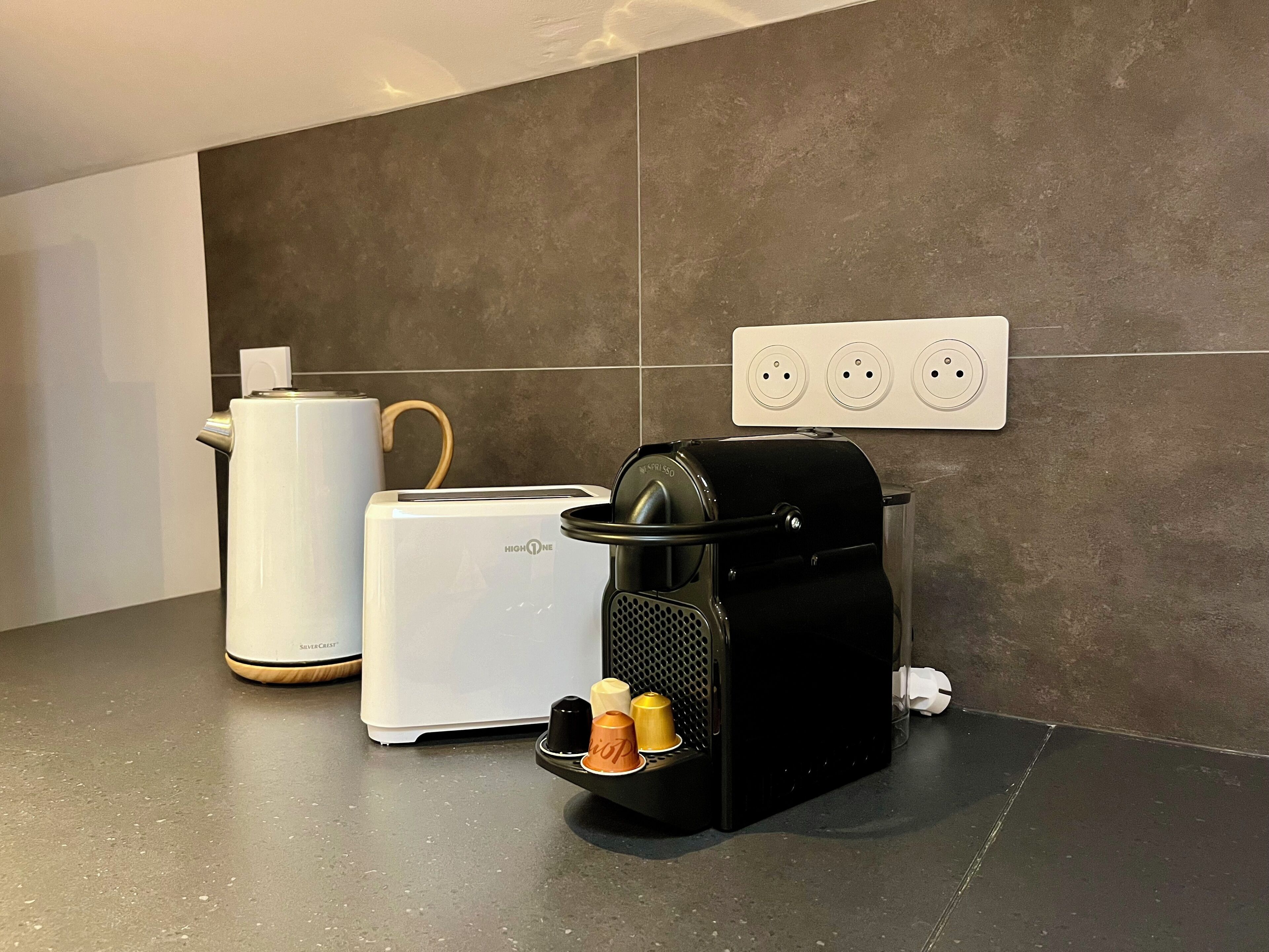 Cozinha com cafeteira, torradeira e eletrodoméstico preto com suporte para cápsulas de café.