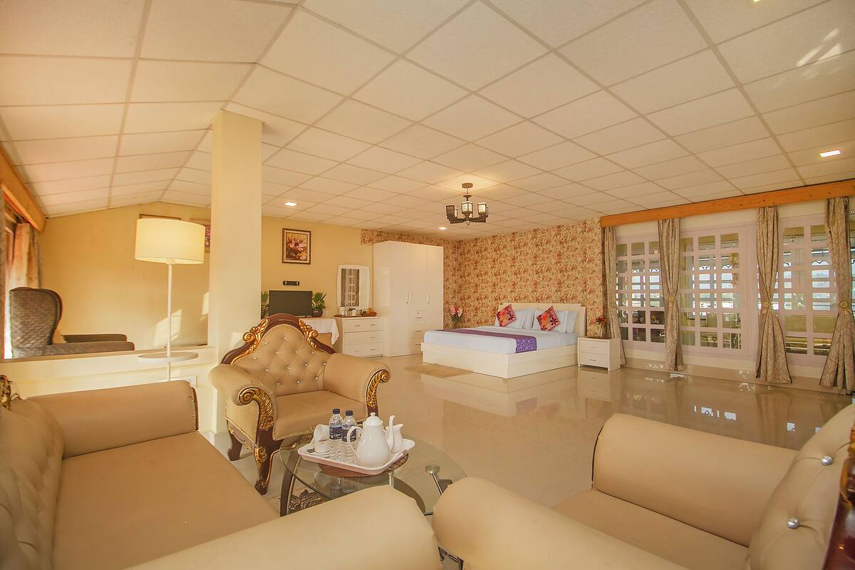 Una habitación de hotel con una cama grande, dos sofás, una mesa de centro con una bandeja de objetos, un televisor y un candelabro.