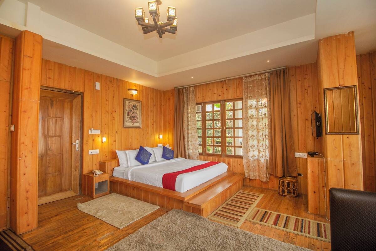 Un dormitorio con paneles de madera, una cama, mesitas de noche, un candelabro, una ventana con cortinas y un espejo en la pared.