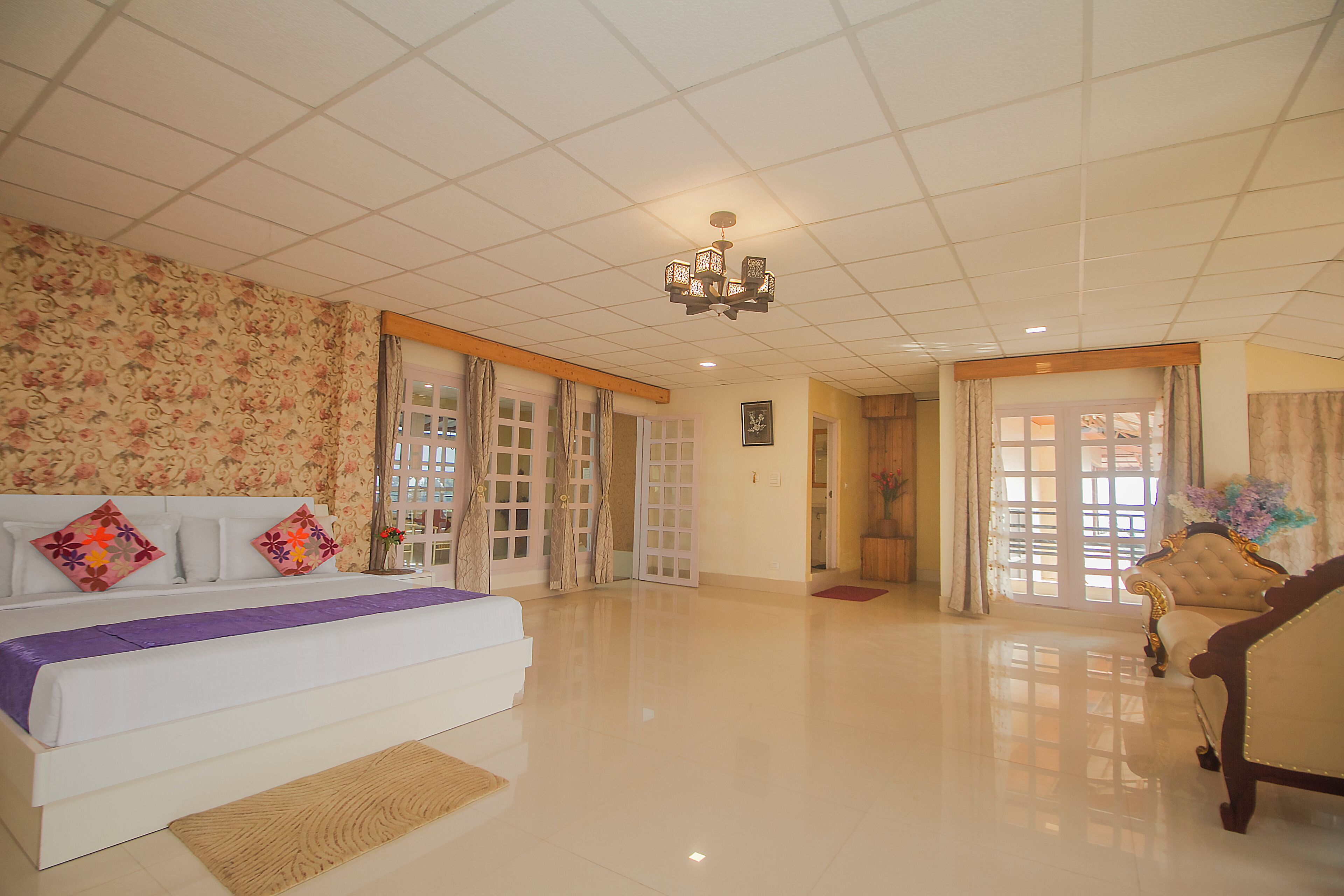 A spacious hotel room with a large bed, a chandelier, and a sitting area with a sofa.