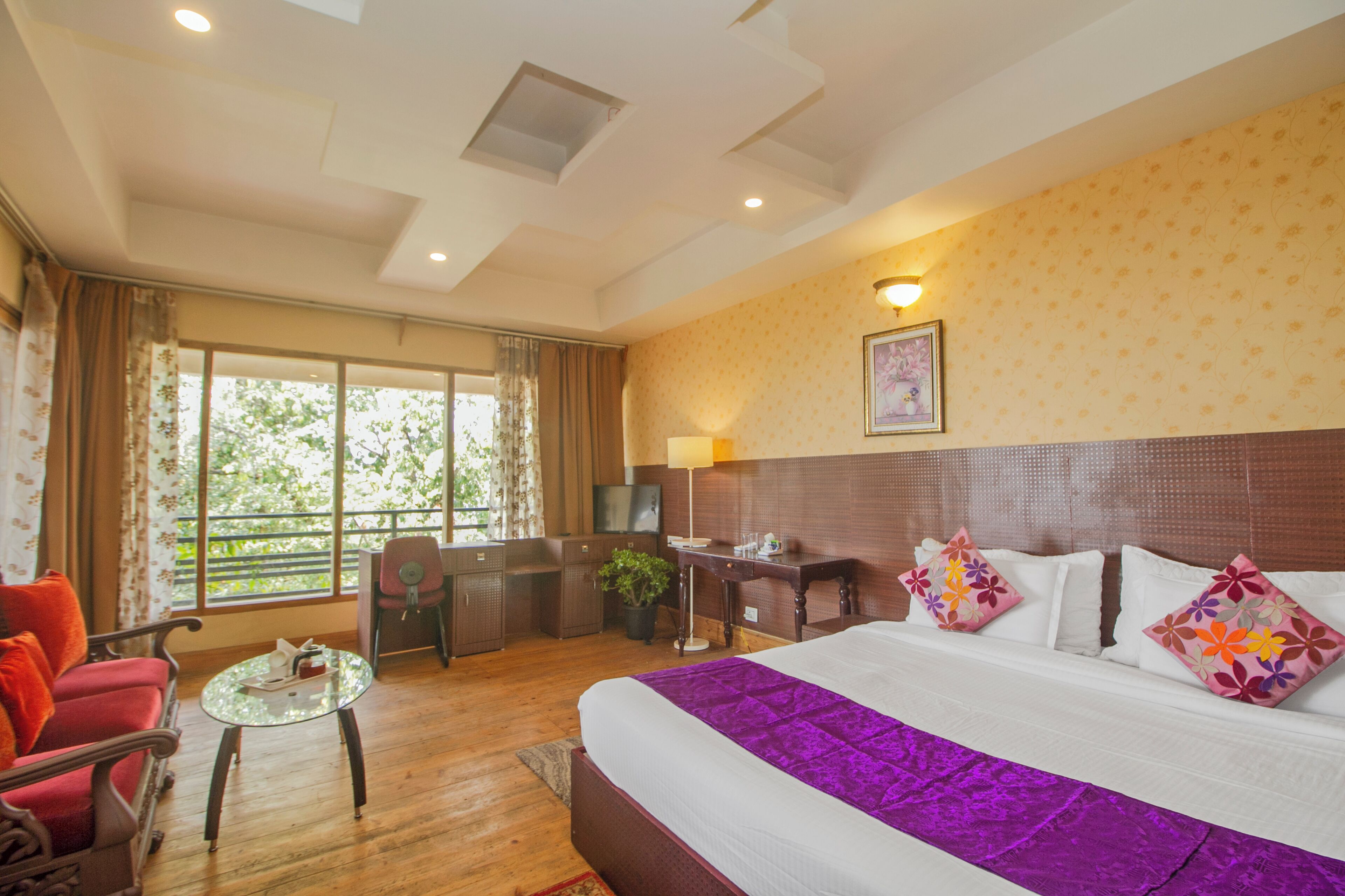 A hotel room with a large bed, a desk, a chair, and a window with a view of greenery.