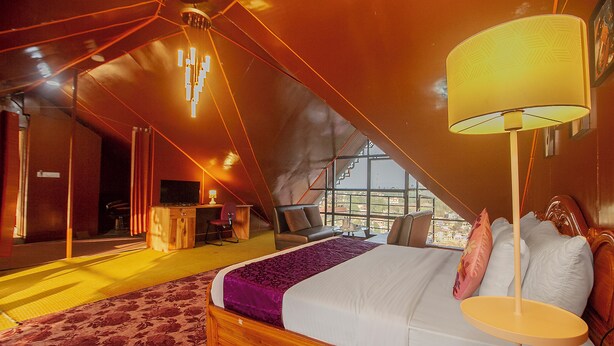 Un dormitorio con una cama grande, una mesita de noche y vistas al exterior a través de un amplio ventanal.
