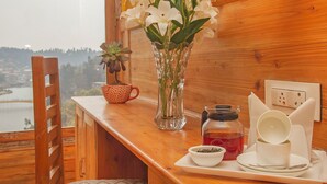 Un interior de madera con vista a un lago, un jarrón con flores blancas, una taza roja y un juego de té en una bandeja.