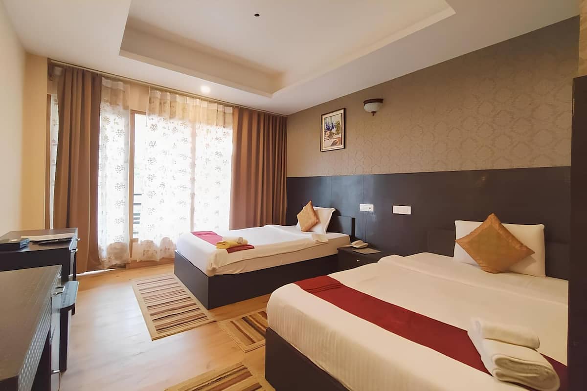 Habitación de hotel con dos camas, un escritorio y un ventanal grande con cortinas.
