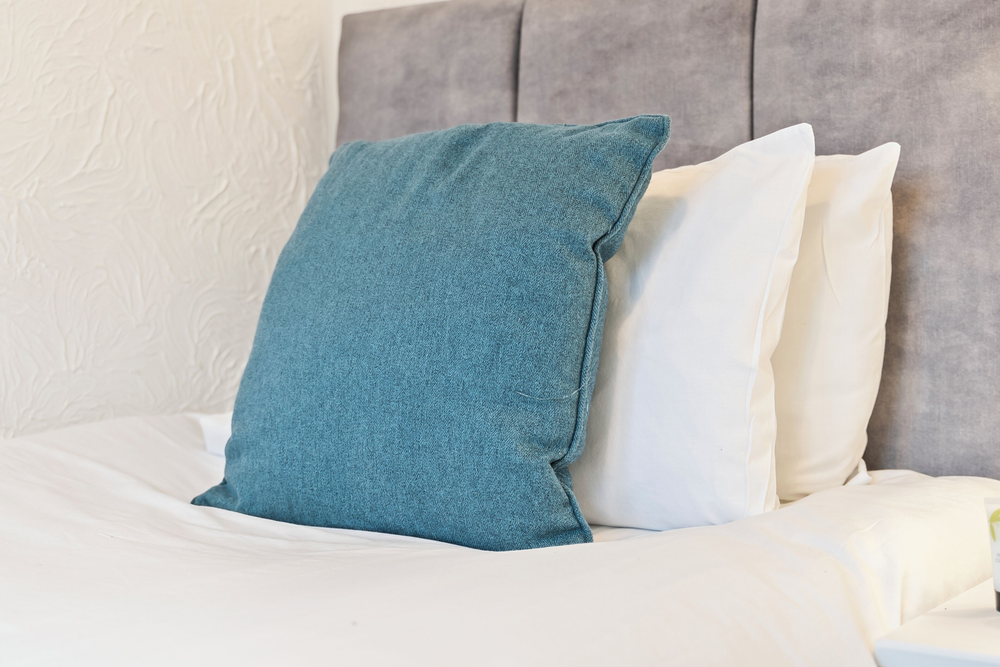 Un lit avec une literie blanche et un oreiller de couleur turquoise.
