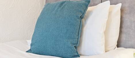 Un lit avec une literie blanche et un oreiller de couleur turquoise.