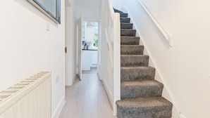 A hallway with a carpeted staircase leading to a kitchen area. - Spacious 3-bed House in Birmingham (Birmingham)