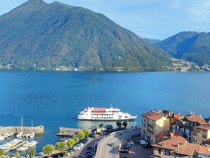 A waterfront city with a large mountain in the background, a ferry dock, and a mix of residential and commercial buildings. - Dream Vacation (Argegno)