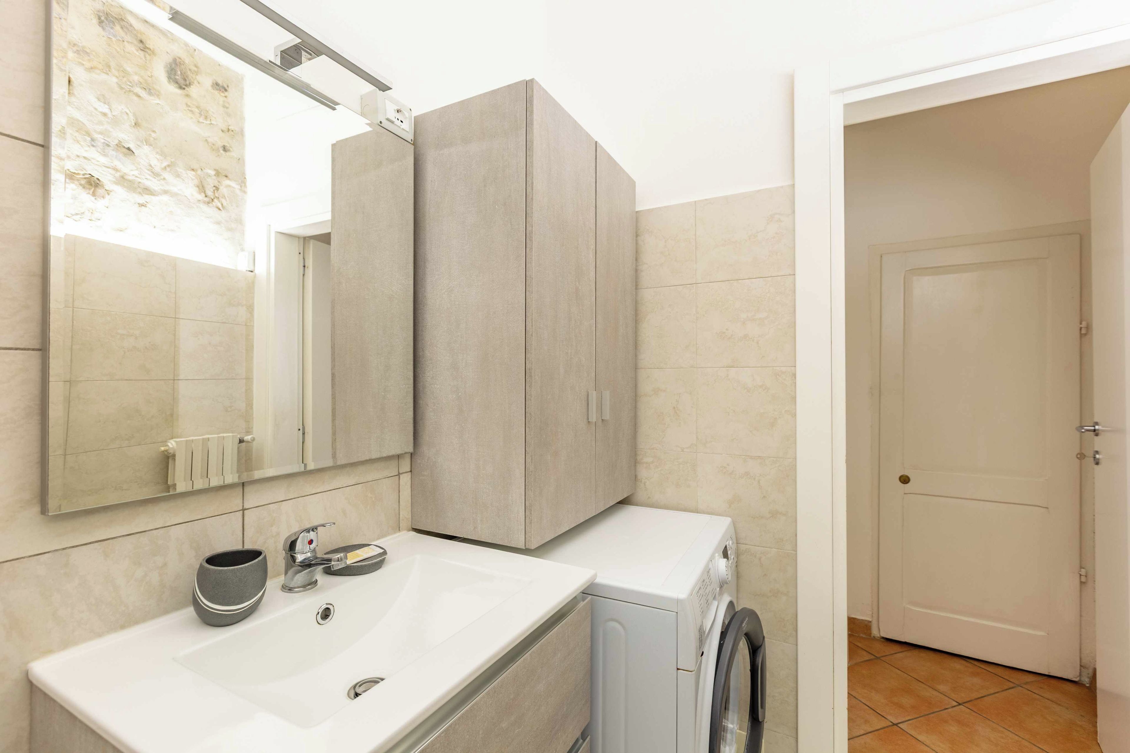A bathroom with a white sink, a mirror, a towel rack, a cabinet, and a washing machine.