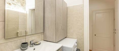 Une salle de bain avec un lavabo blanc, un miroir, un porte-serviettes, un meuble et un lave-linge.