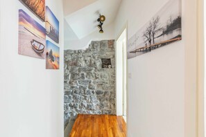 A hallway with a stone wall, wooden flooring, and artwork on the walls. - Dream Holiday  (Argegno)