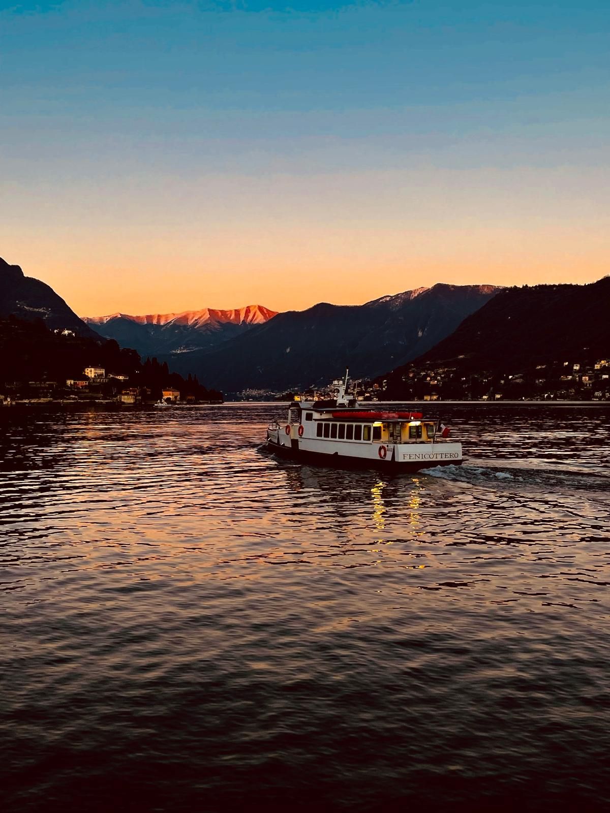 Un bateau nommé « FENICOTTERO » navigue sur une étendue d’eau, avec des montagnes en arrière-plan.