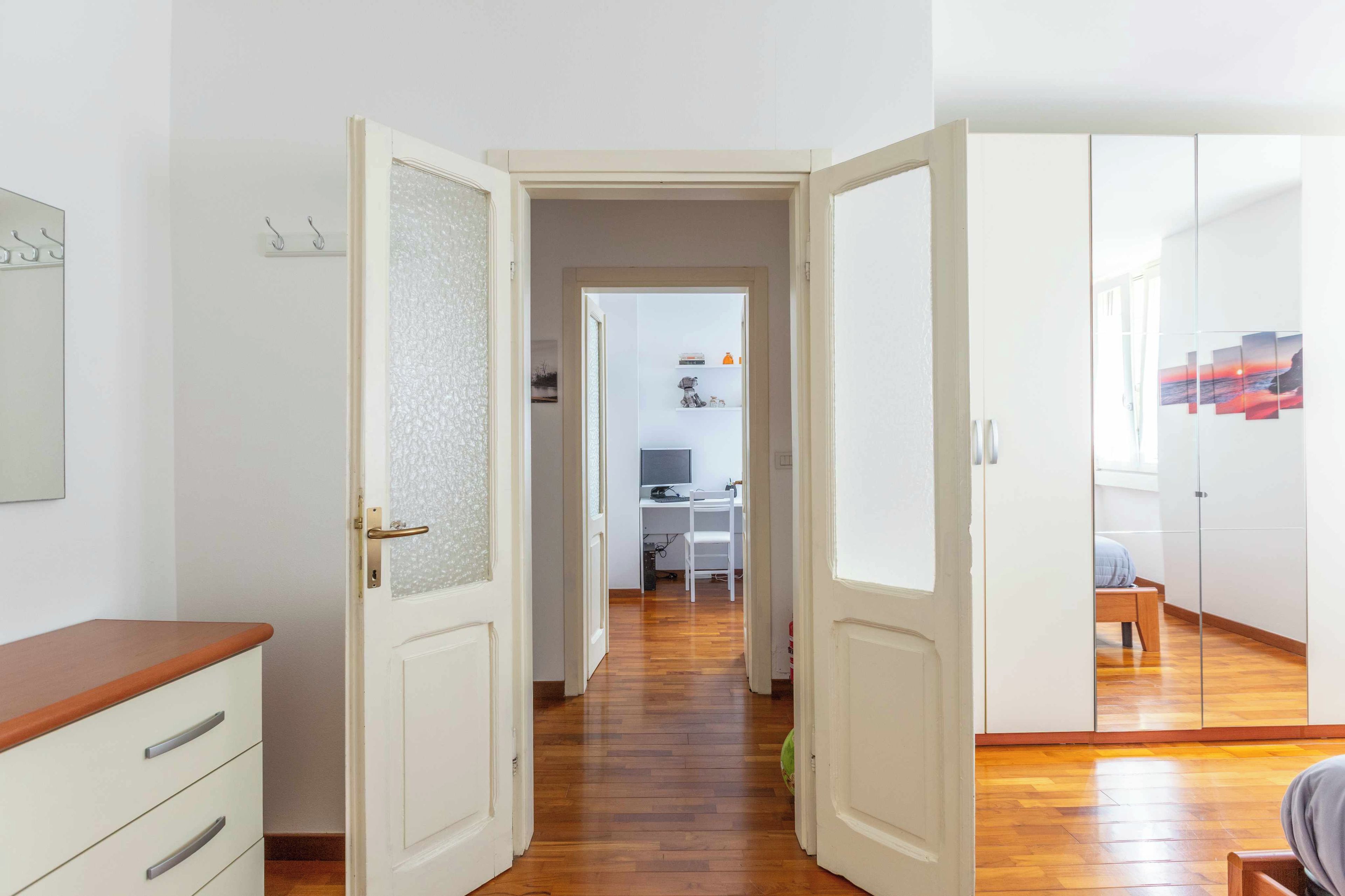 Ein Flur mit Holzboden, der zu einem Zimmer mit Schreibtisch und Stuhl, einem Kleiderschrank und einer Tür mit satinierten Glasscheiben führt.