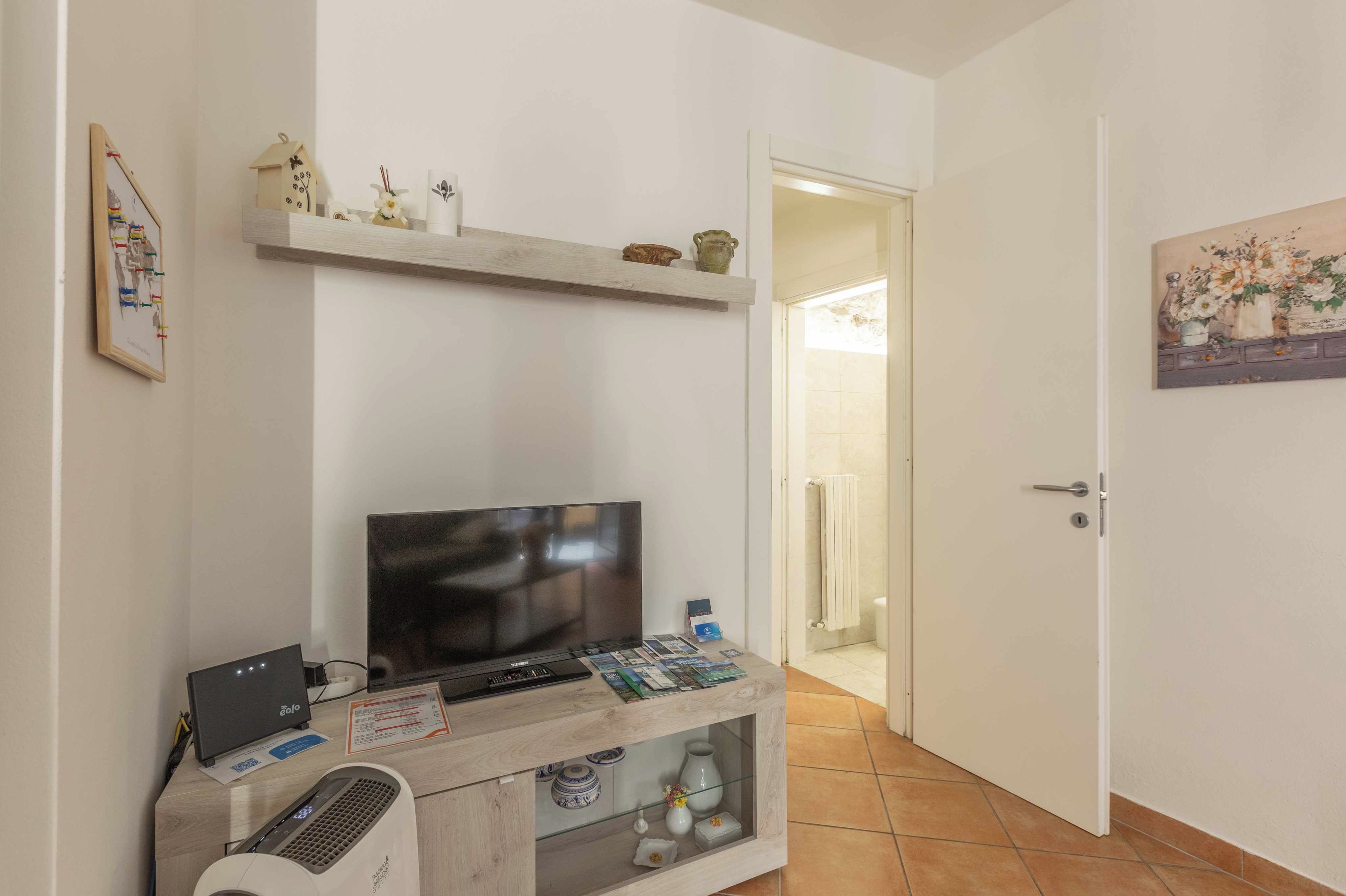 Ein Zimmer mit Fernseher, einem kleinen Schrank mit Fernbedienung und einer Tür zum Badezimmer.
