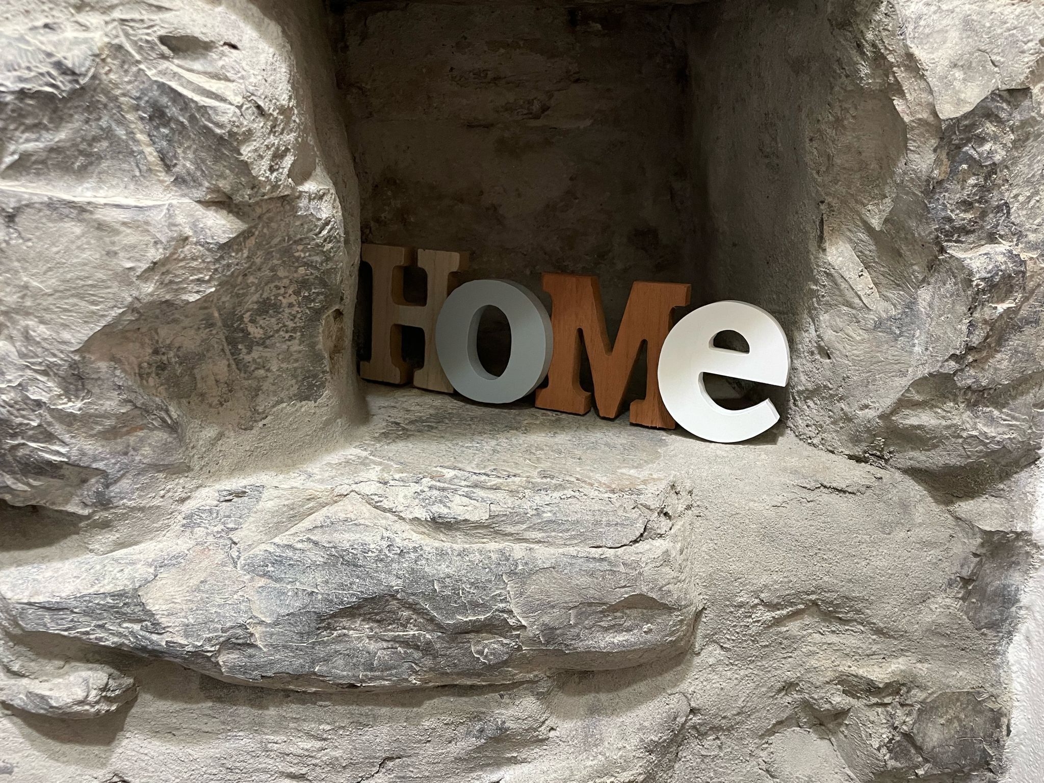 Eine Steinmauer, auf der das Wort „HOME“ mit Holzlettern steht.