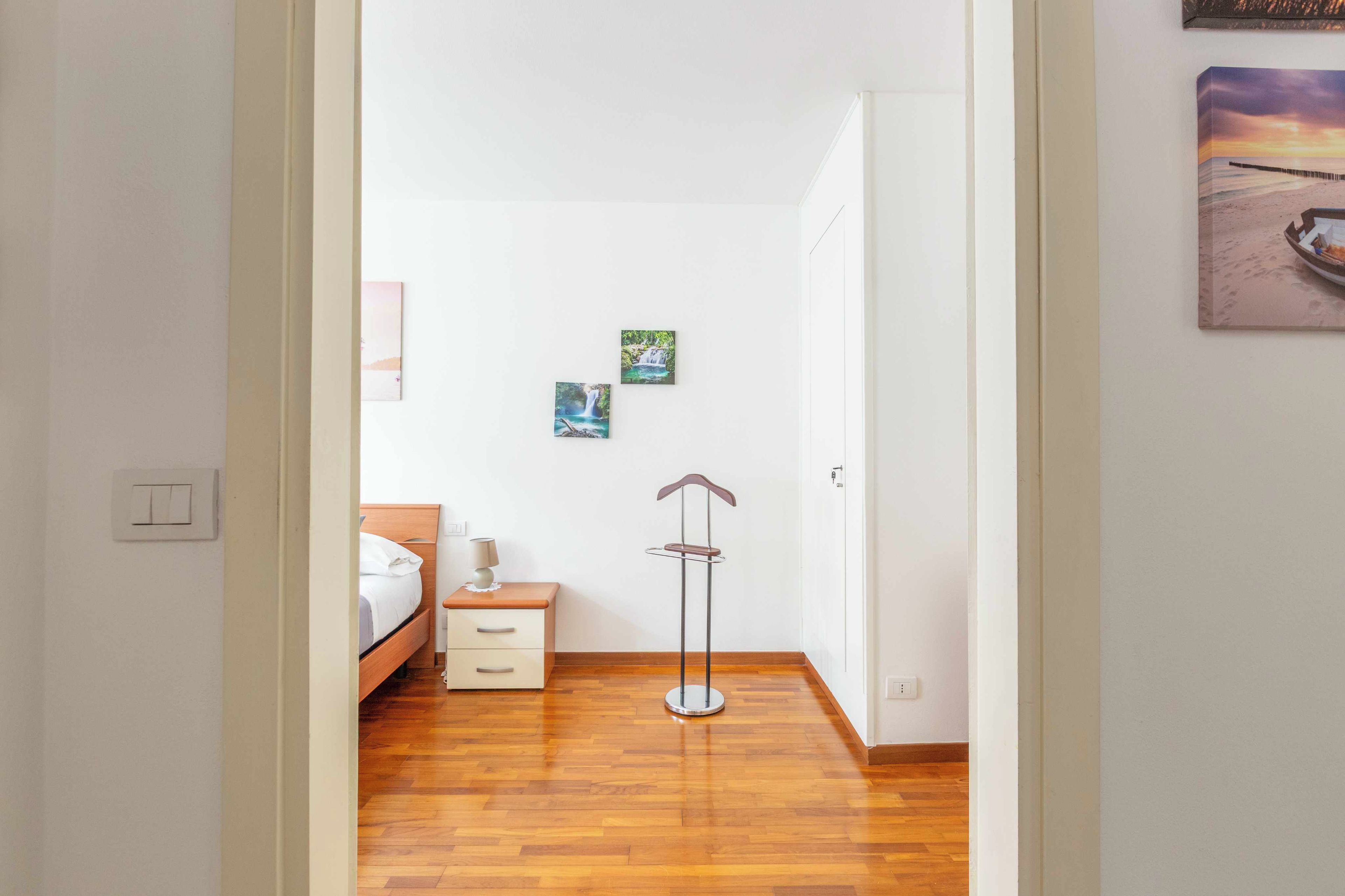 Une chambre avec un plancher en bois, un lit, une table de chevet, une lampe et deux tableaux accrochés au mur.