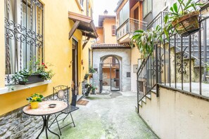 A narrow courtyard with a tiled floor, a round table with chairs, and potted plants. - Dream Vacation (Argegno)