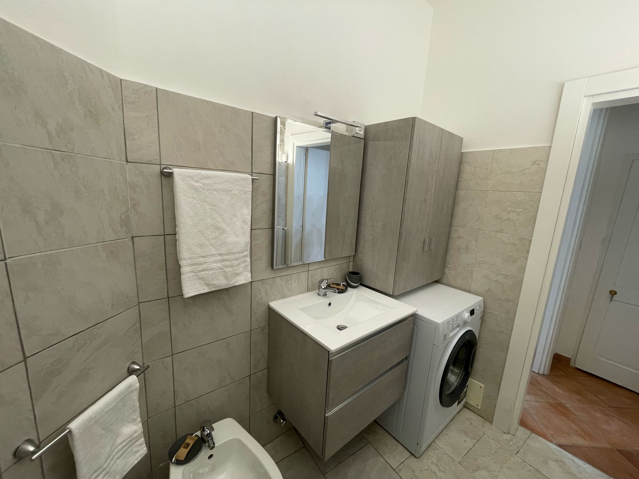 Un baño moderno con lavamanos, espejo y lavadora integrada.