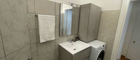 Un baño moderno con lavamanos, espejo y lavadora integrada.