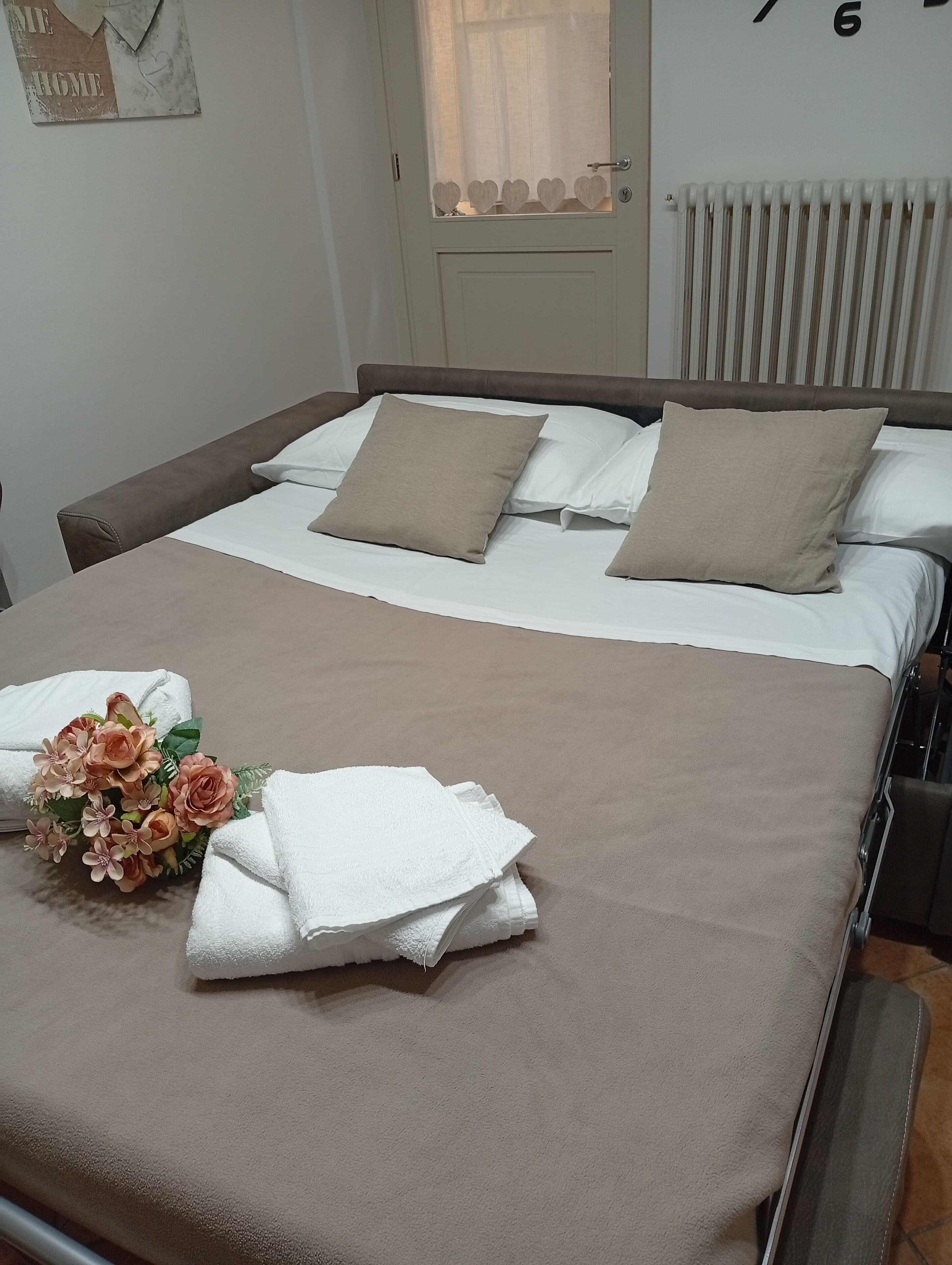 Un lit bien fait, avec une couverture marron, des oreillers blancs et un bouquet de fleurs.