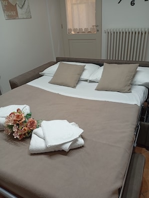 Una cama bien tendida con una colcha marrón, almohadas blancas y un ramo de flores.