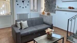 A living room with a grey sofa, a wall clock, a small table with a vase, and a stone wall. - Dream Holiday  (Argegno)