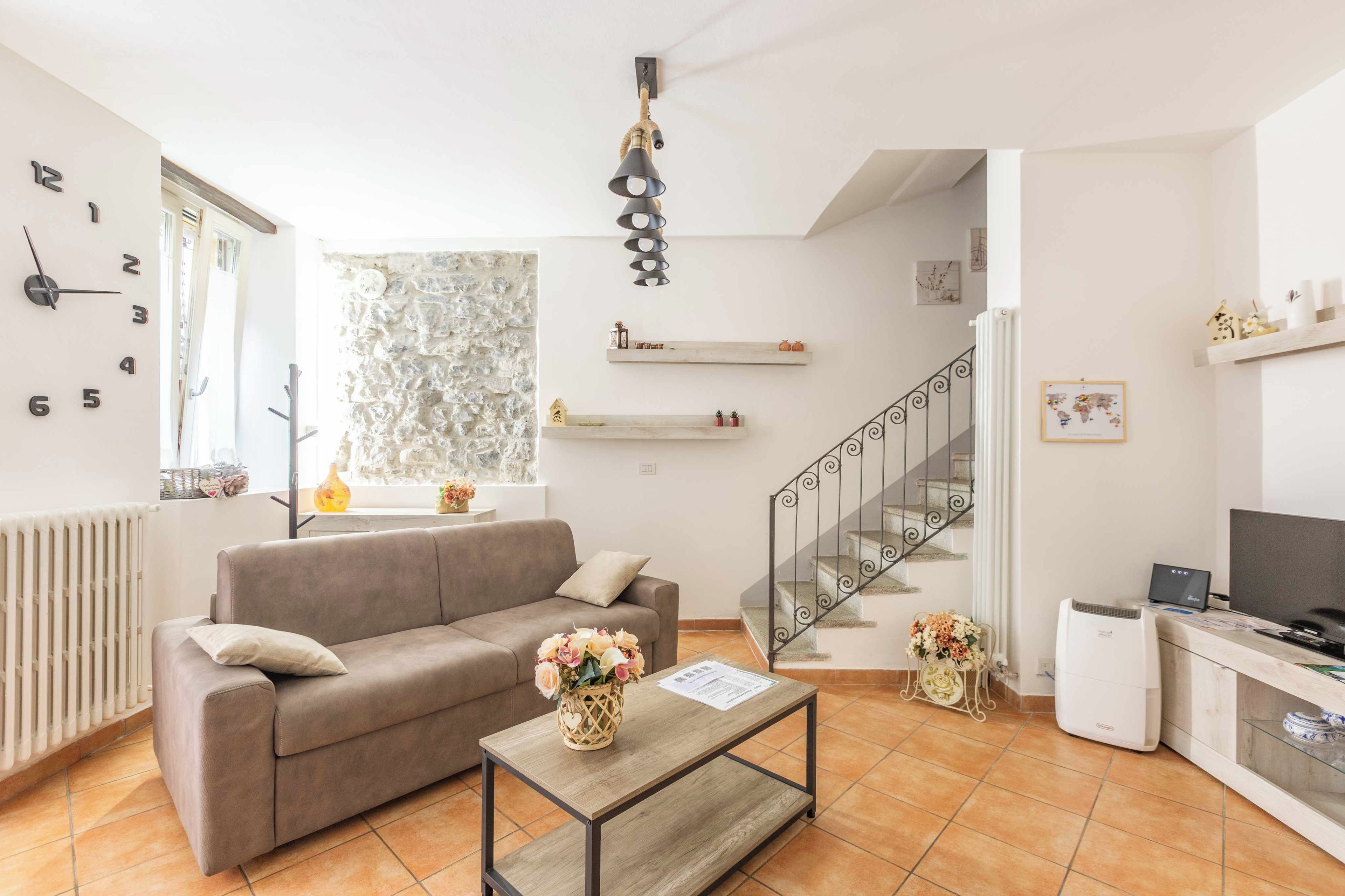 A living room with a sofa, a coffee table with a vase, a staircase, and a TV.