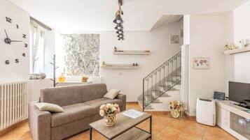A living room with a sofa, a coffee table with a vase, a staircase, and a TV.