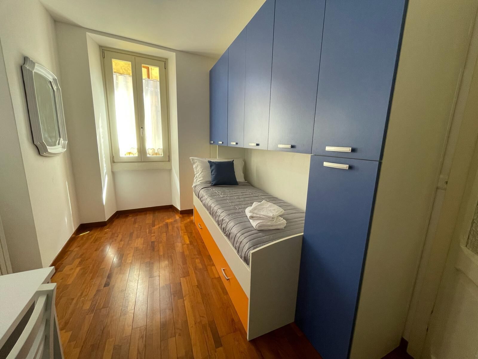 Une chambre à coucher de taille modeste, avec un lit, une fenêtre avec des rideaux et une armoire bleue.