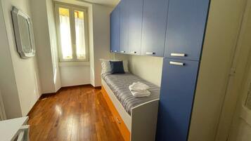 Une chambre à coucher de taille modeste, avec un lit, une fenêtre avec des rideaux et une armoire bleue.