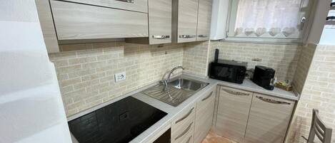 A compact kitchen with a black induction cooktop, a sink, and a microwave.