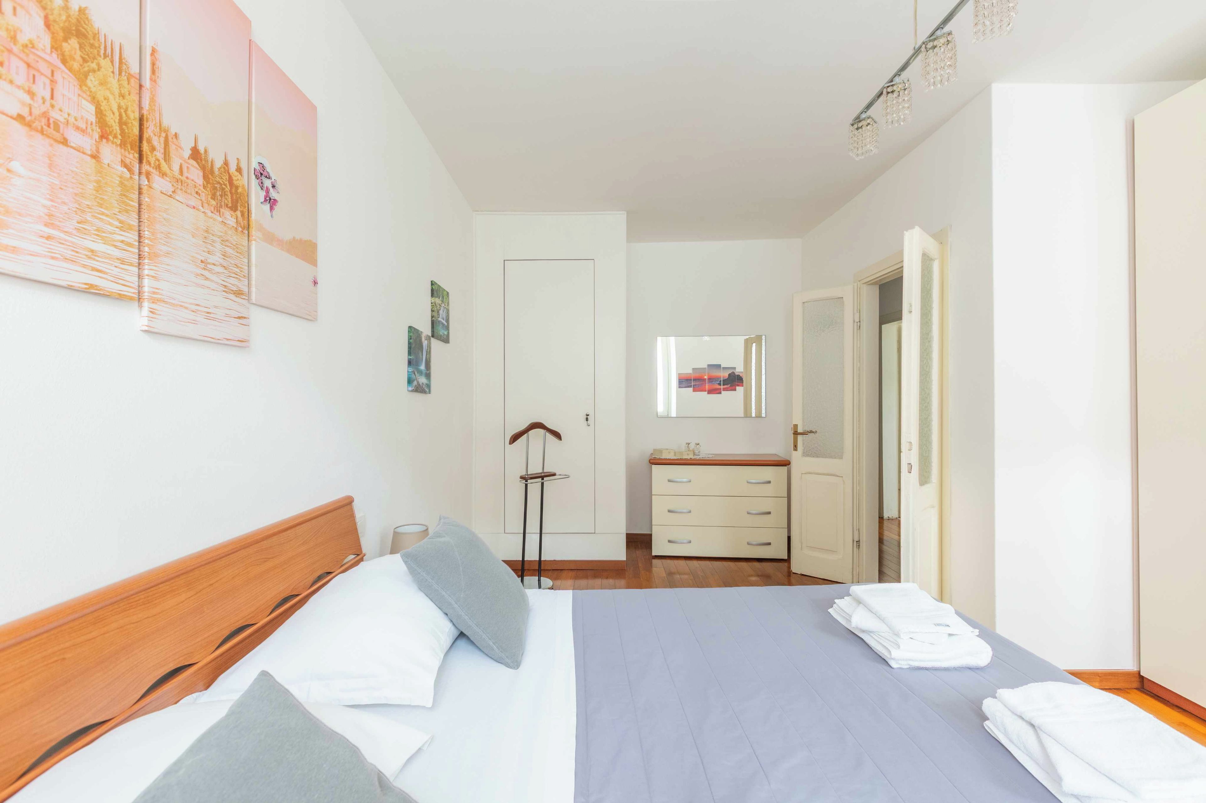 Une chambre d’hôtel comprenant un lit, une table de chevet, un miroir, une armoire et une porte donnant sur une autre pièce.