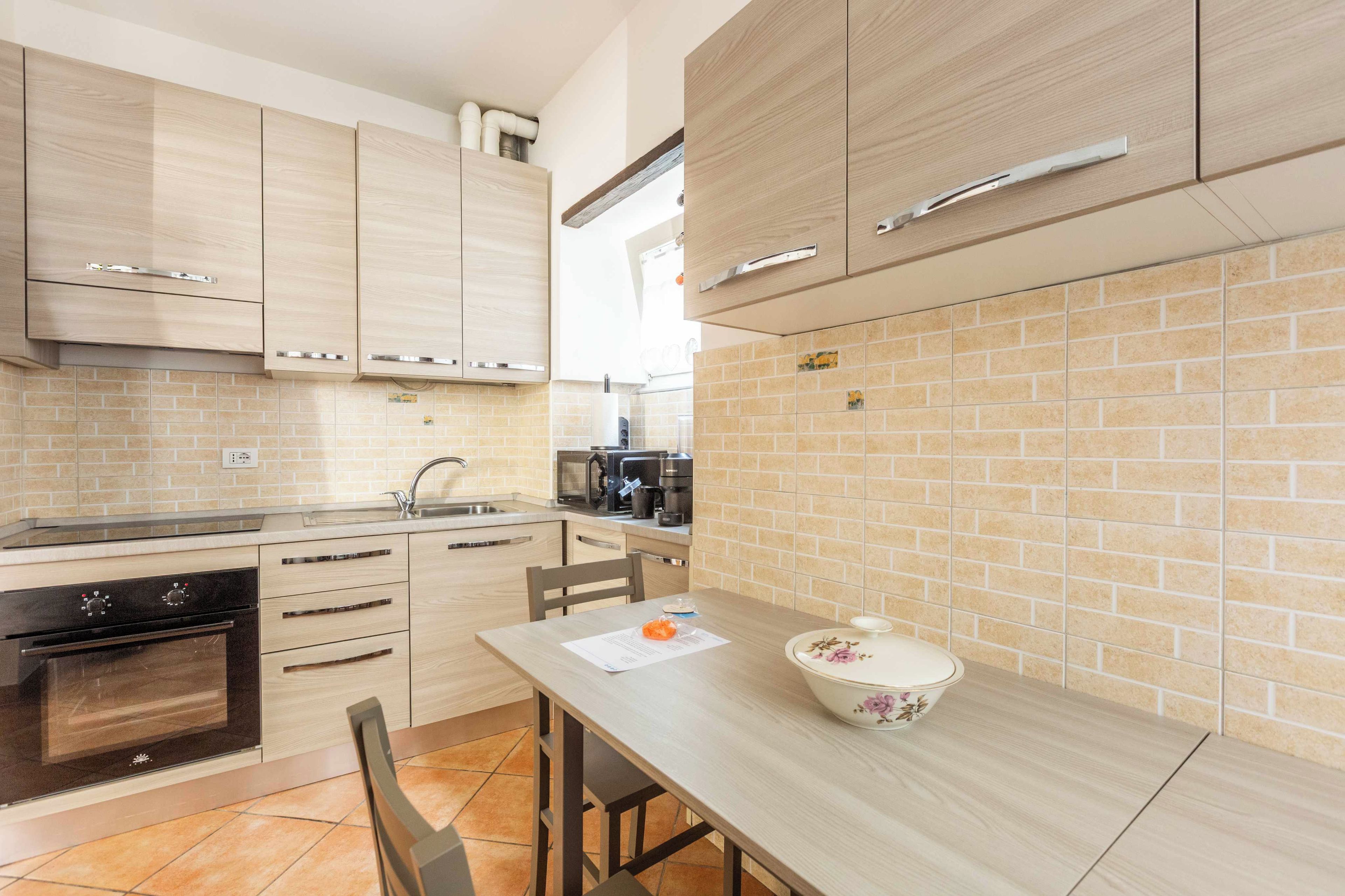 A modern kitchen with wooden cabinets, a built-in oven, and a dining area with a table and chairs.