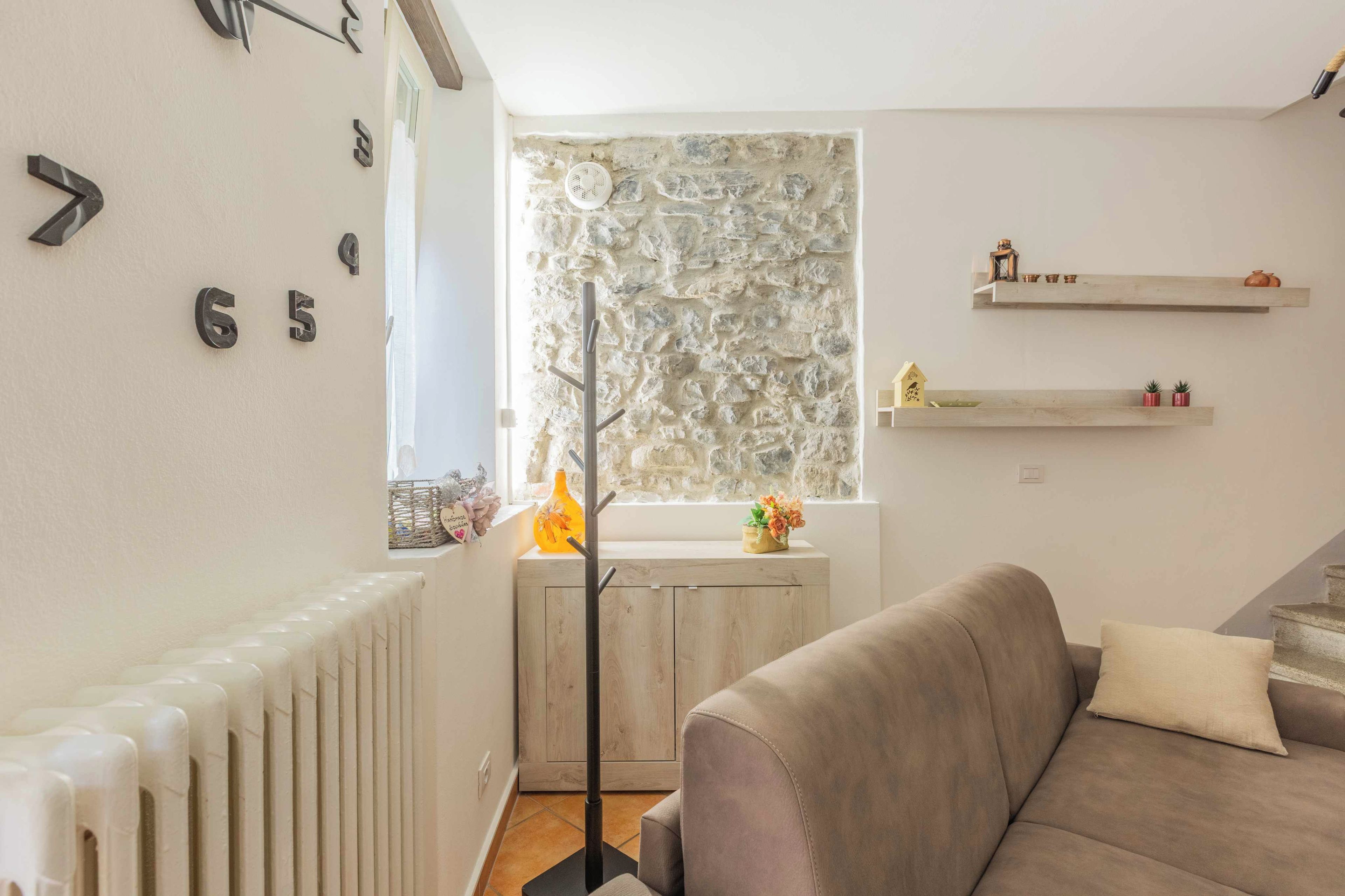 Sala de estar com parede de pedra, radiador, sofá e janela com vista para o exterior.