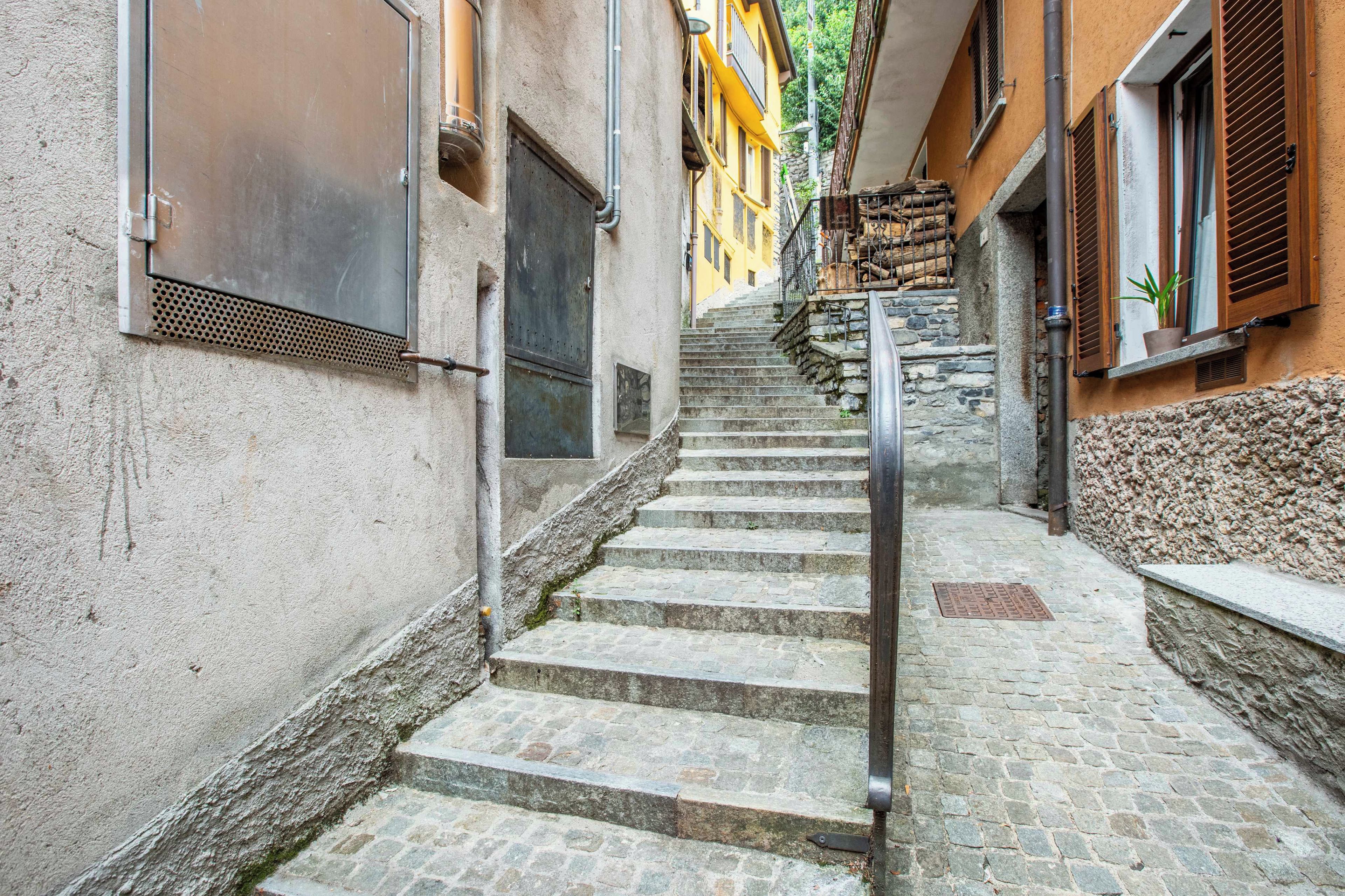 A narrow stone staircase leading up to a building with a metal handrail.