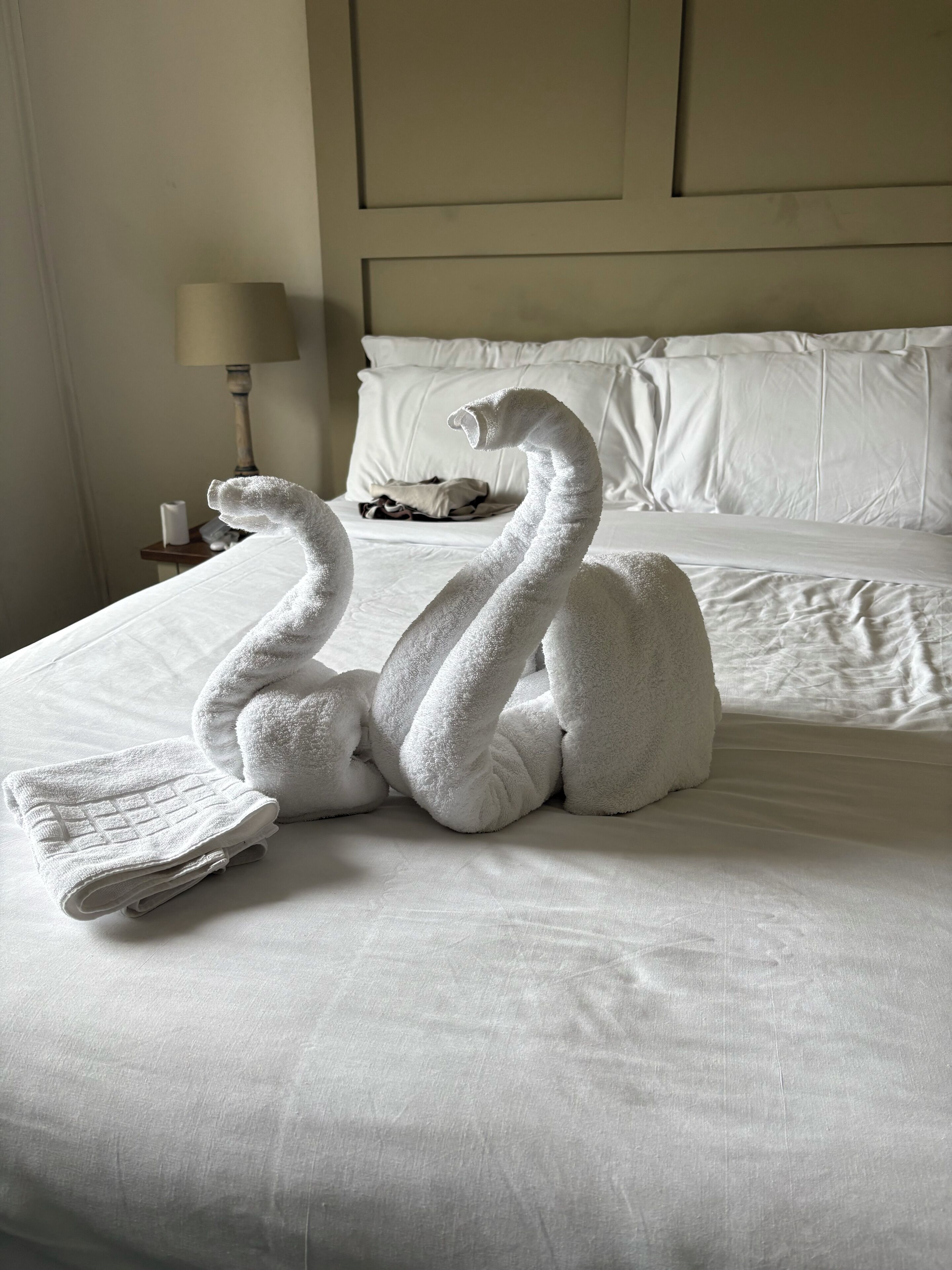 Una cama con ropa blanca y dos toallas con forma de cisne.