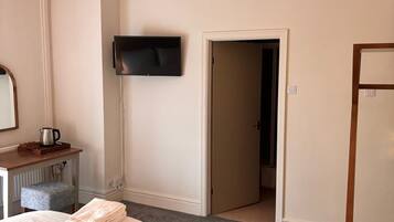 Habitación de hotel con una cama, un televisor de pantalla plana montado en la pared, una puerta que da a otra habitación y una mesita con una tetera.