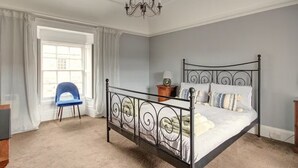 A bedroom with a four-poster bed, a chandelier, a chair, and a window with curtains.
